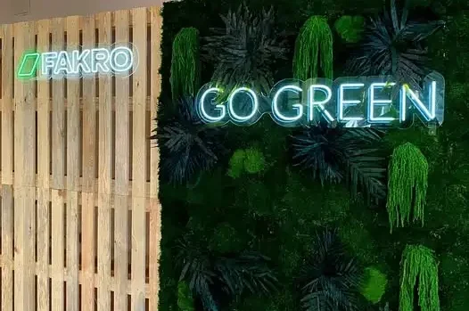 Zielona ścianka reklamowa z neonem "GO GREEN" i logo FAKRO wykonana przez firmę Grafion Reklamy – połączenie naturalnych dekoracji z podświetlanym logo.